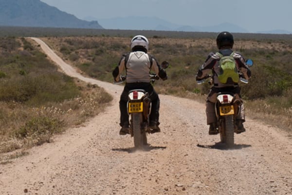 Two riders on a dirt road in the East African bush